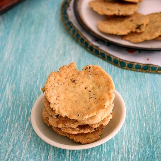 Stack of mathris on a small plate with a tray of cookies in the background on a blue surface.