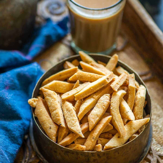 Bowl of crispy snacks next to a glass of tea on a wooden tray